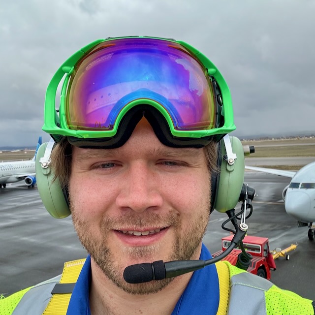 Profile picture showing a person wearing green ski goggles and headphones at an airport